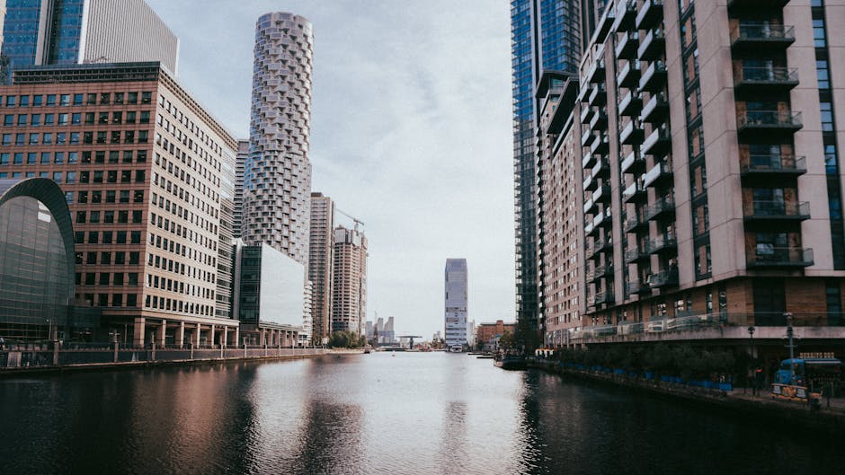 A skyline view of Canary Wharf featuring modern skyscrapers, including a tall reflective glass tower in the center, surrounded by other high-rise office buildings with varying architectural styles suc